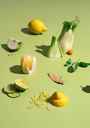 Sitron, lime, eple, mynte, laurbærblad og en fennikel mot syrlig grønn bakgrunn.